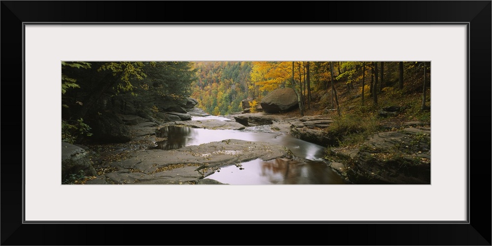 Panoramic photograph focuses on the edge of a stream filled with large rocks before it falls over a cliff and crashes agai...