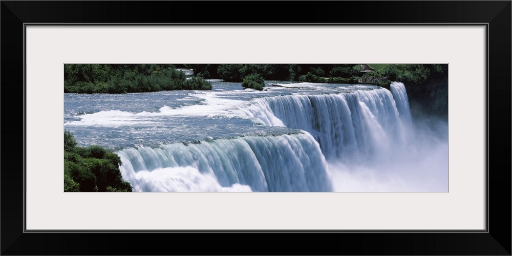 A large panoramic photograph taken of Niagara falls with trees and foliage lining the back of the picture.