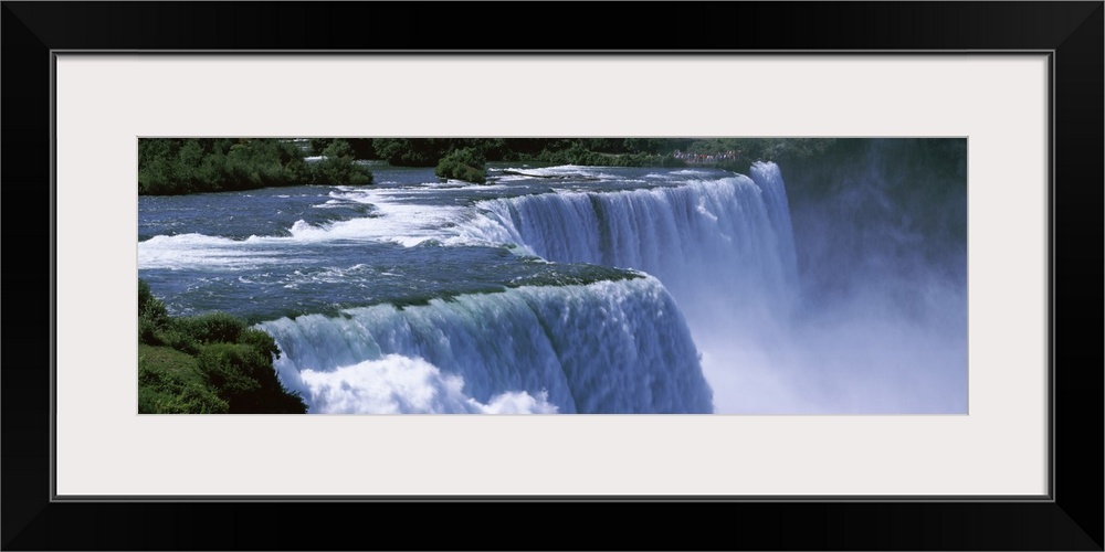 Panoramic photo of a water rushing over a waterfall with mist coming up from the bottom.