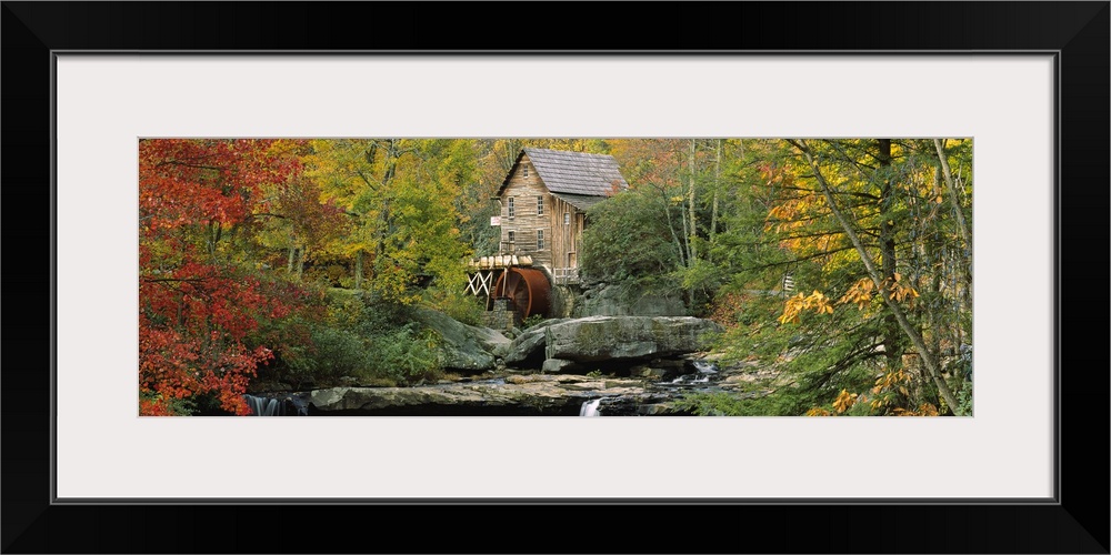 Panoramic photograph of mill in forest surrounded by fall foliage.