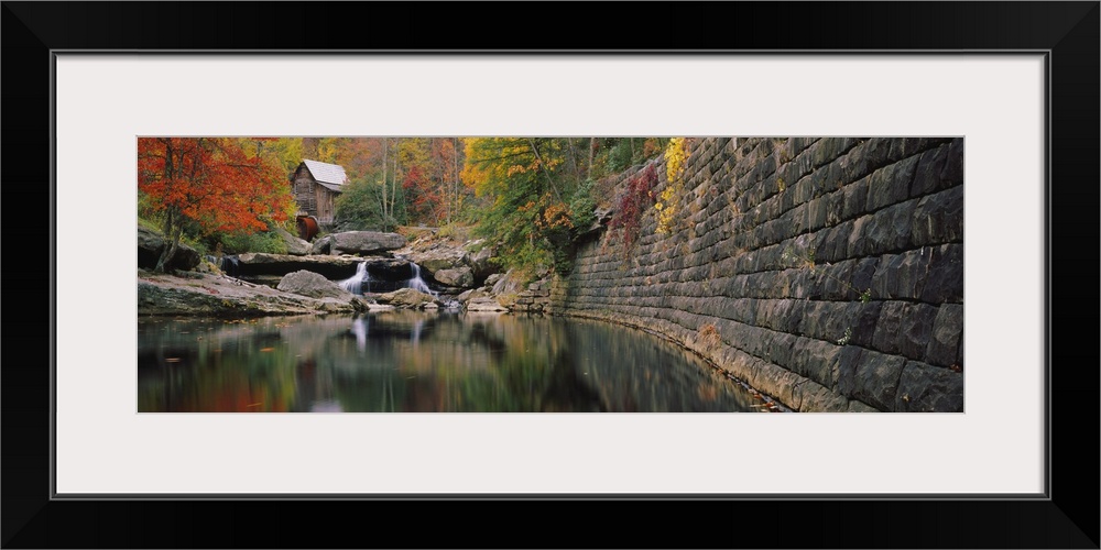 Panoramic photo of a lake with a mill in the distance surrounded by fall foliage.