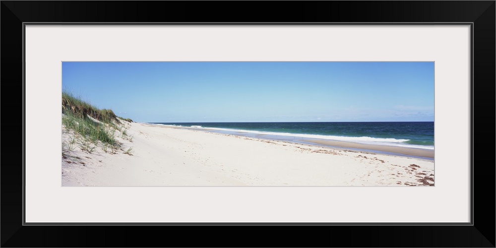 Panoramic photograph taken of the beach with the sand dunes just to the left and the ocean water coming up onto the sand.