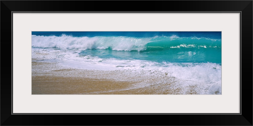 Panoramic photograph of water crashing onto the sand and being swept back out to sea.