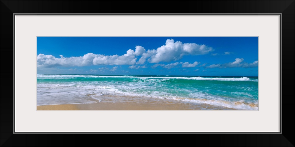 Panoramic view of a Hawaiian beach where waves are washing up on the shore while the wind blows cumulus clouds across an o...