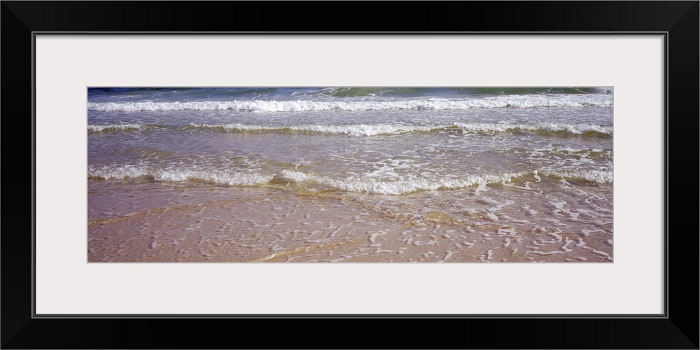 Giant, landscape photograph of small waves rolling onto the shore, covering the sand, in the Gulf of Mexico.