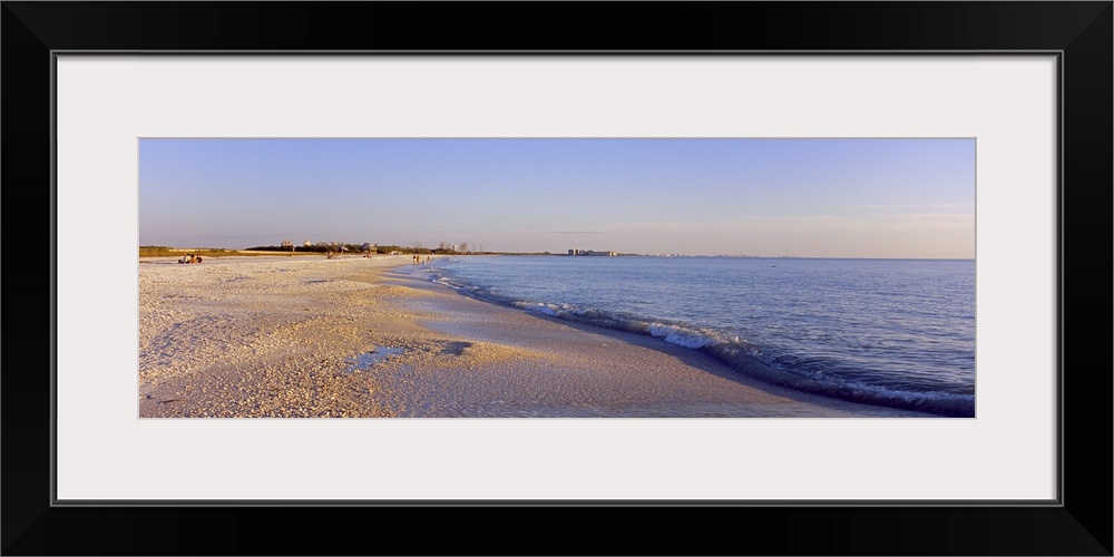 Panoramic photograph looking down the shoreline of Fort Myers Beach beneath a blue sky, in the Gulf of Mexico, Florida.
