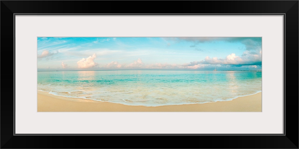A wide angle panoramic wall hanging of a calm tropical ocean, waves on the beach, and cumulus clouds near the horizon.