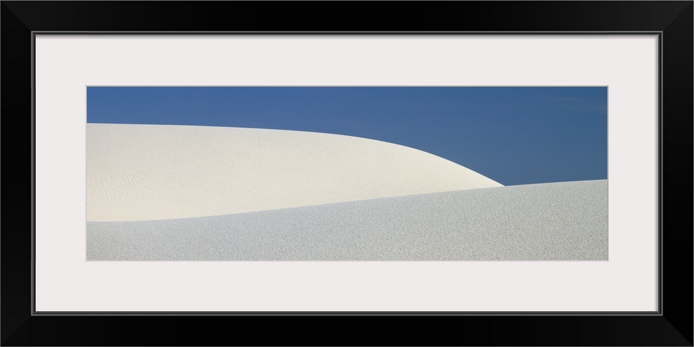 Panoramic photograph of the sloping dunes of White Sands, New Mexico, contrasting with the darker sky, creating a minimali...