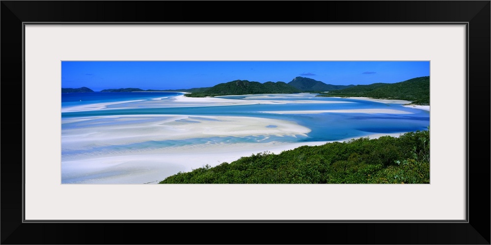 Panoramic view of white beaches and water surrounded by hills and dense forest.