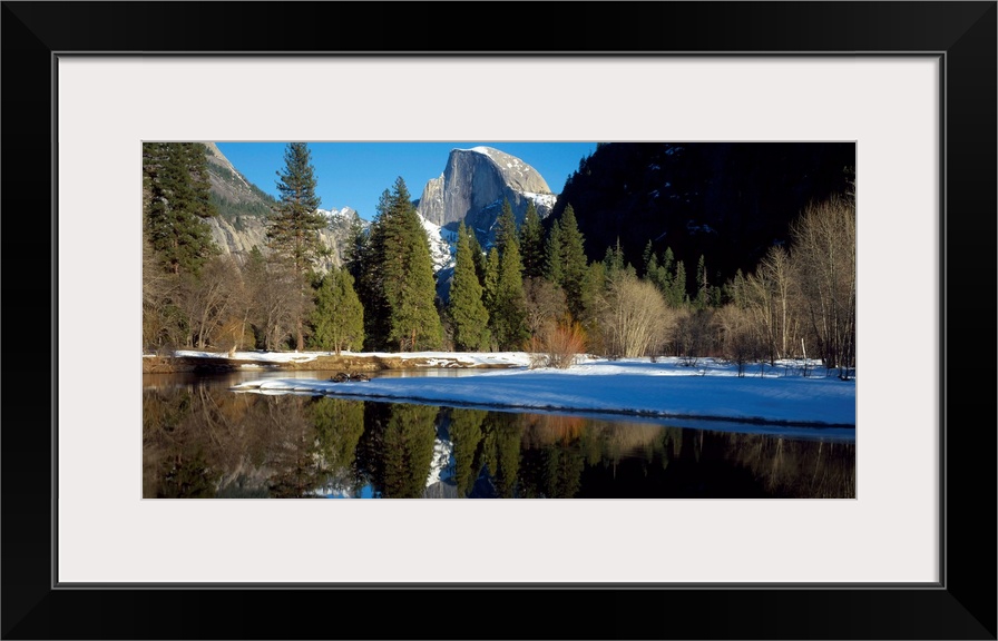 This picture is taken of Yosemite during winter with trees lining the water and a view of a mountain in the background.
