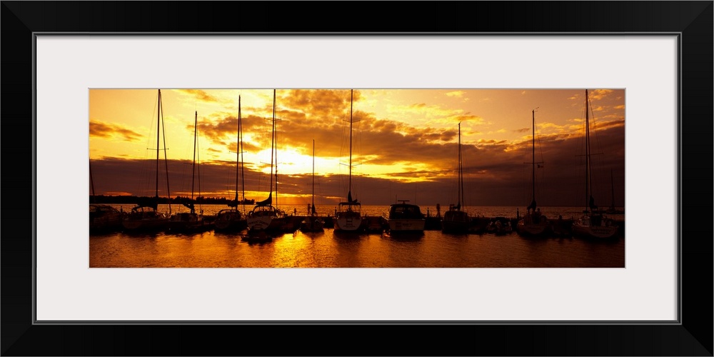 Panoramic photograph of many boats in a line, docked in Egg Harbor beneath a vibrant setting sun, in Door County, Wisconsin.