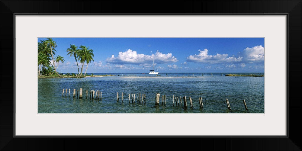 Wooden posts in the sea with a boat in background, Laughing Bird Caye, Victoria Channel, Belize