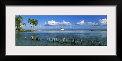 Wooden posts in the sea with a boat in background, Laughing Bird Caye, Victoria Channel, Belize