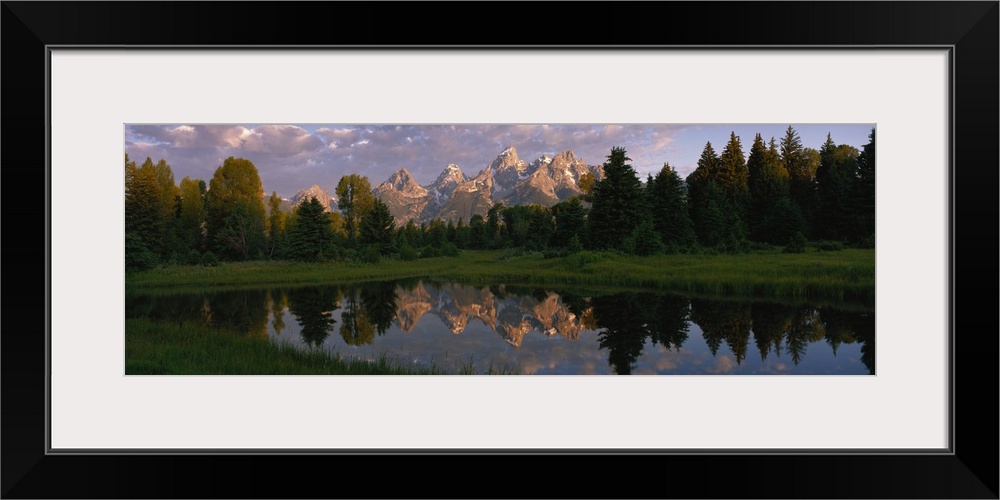 Panoramic photograph of lake with forest in the background and snow covered mountains in the distance under cloudy skies.