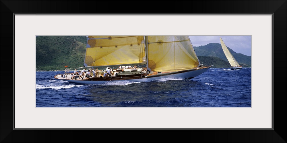 A crowded yacht sails past a tropical island in the Caribbean in this landscape photograph.