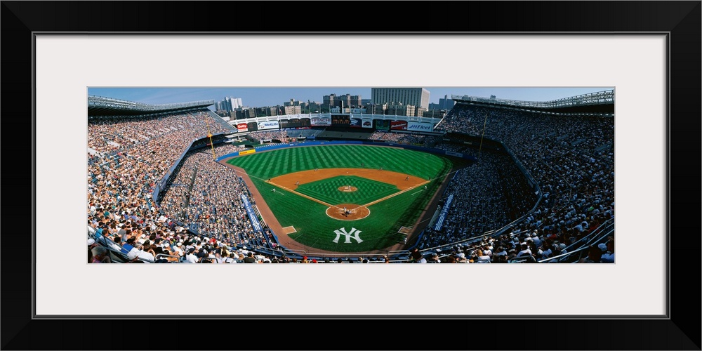 Panoramic photograph taken at Yankee Stadium in the Bronx, New York displays fans enjoying a baseball game on a sunny day....