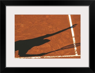 Shadow of tennis player serving on clay court