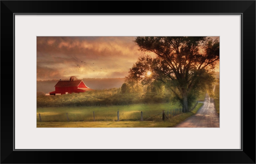 A dirt road in the countryside with a red barn in the distance at sunset.
