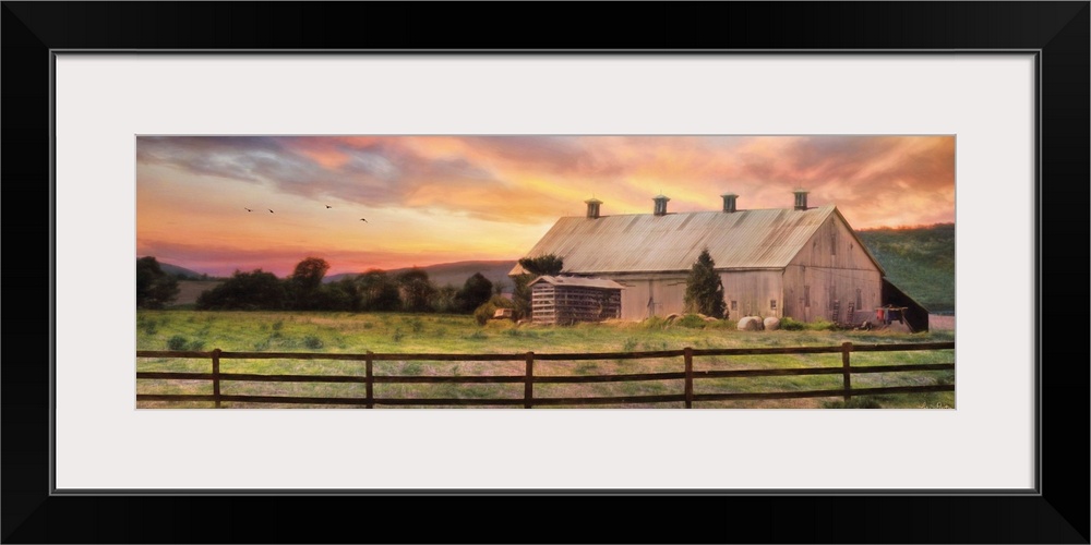 A barn in the countryside with a wooden fence in the early evening.