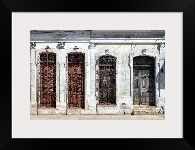 Photograph of an aged Cuban facade with windows and a wooden door.