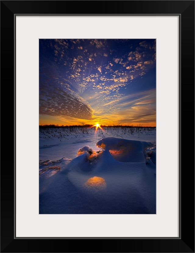 Orange sunset light shining through the clouds onto a snowy field.