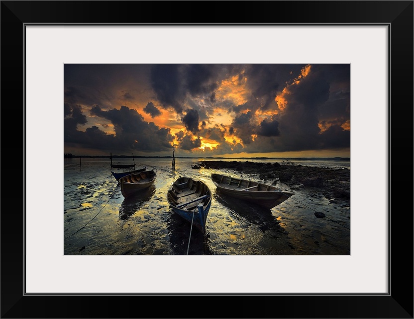 Row boats sitting in still water under dramatic clouds at sunset.