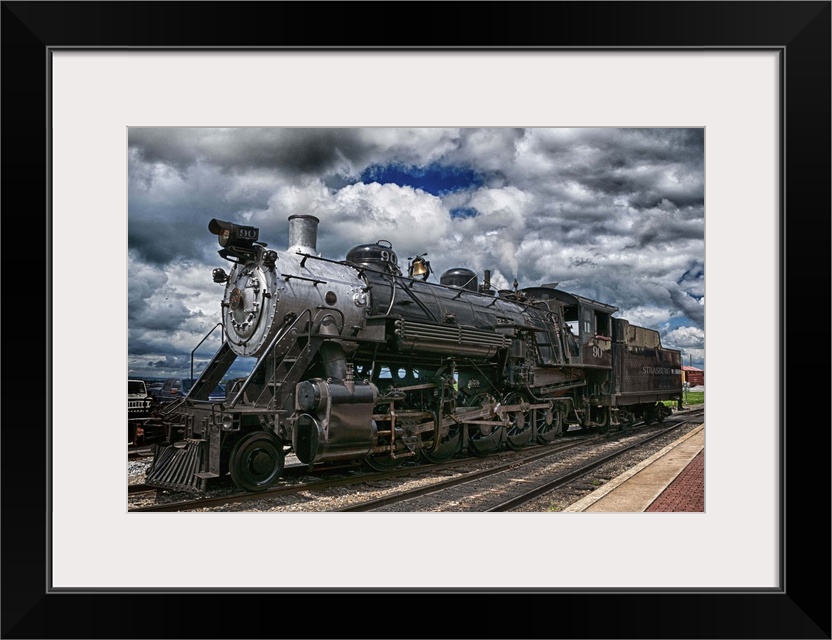 Photograph of an old steam engine sitting on train train under a dramatic cloudy sky.