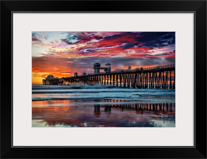 The Oceanside Pier is silhouetted as sunset turns the reflected clouds from yellow to pink to gun metal grey, and finally ...