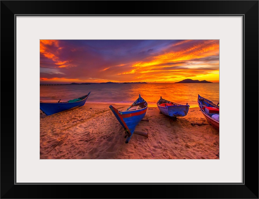 A row of small blue boats resting on the sandy beach with a brilliant sunrise.