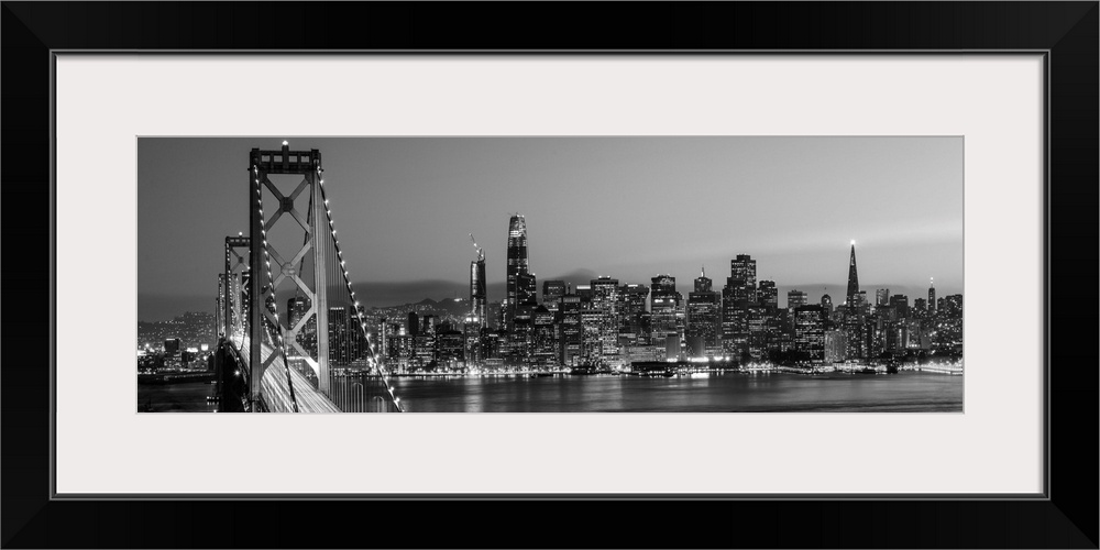 Photograph of the Bay Bridge and the San Francisco skyline lit up at dusk.