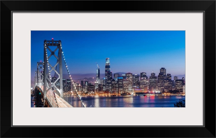 Photograph of the Bay Bridge and the San Francisco skyline lit up at dusk.
