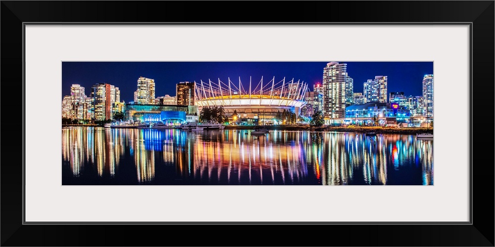 Panoramic photograph of BC Place Stadium and part of the Vancouver skyline lit up at night and reflecting onto the water, ...