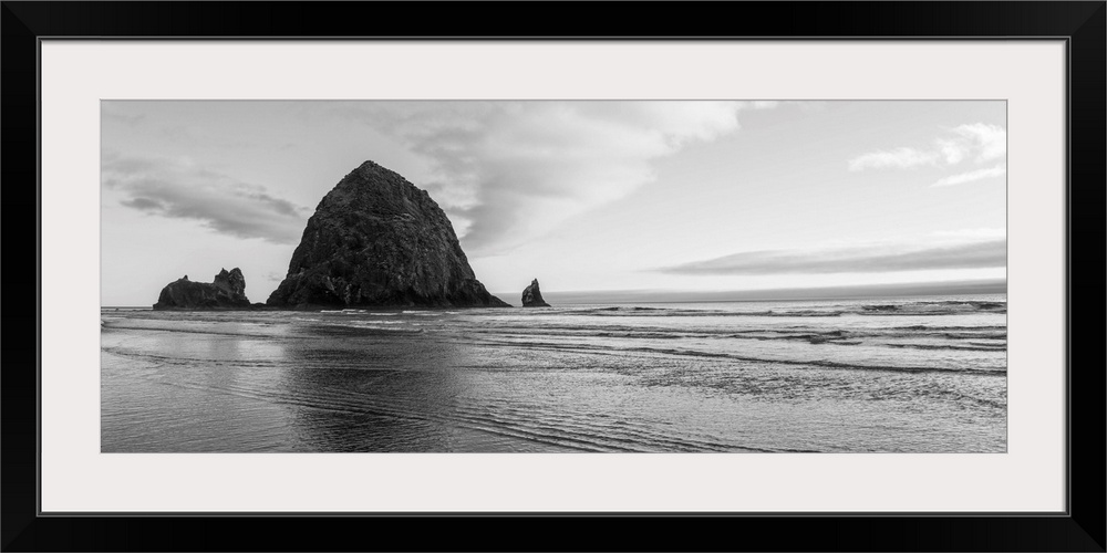 Black and white panoramic photograph of Haystack Rock with rippling waters.