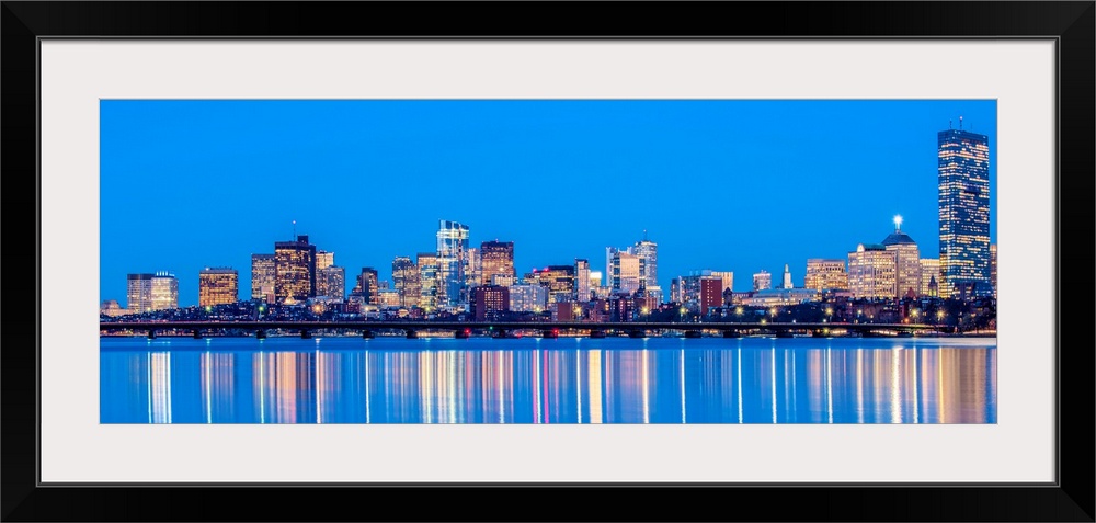 Panoramic view of the Boston City skyline at night, with lights reflected in the water.