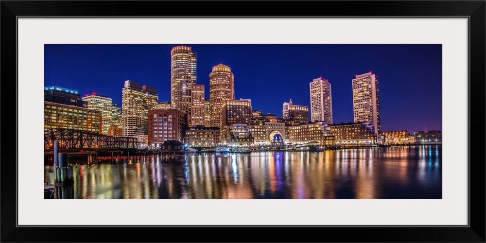 Panoramic view of the Boston City skyline at night, with lights reflected in the water.