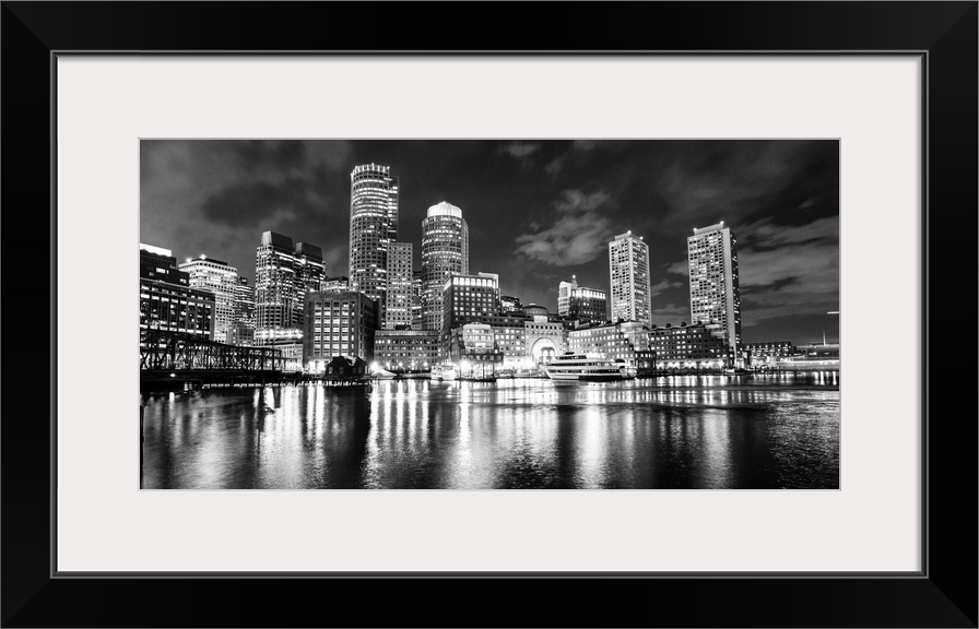 Panoramic view of the Boston City skyline at night, with lights reflected in the water.