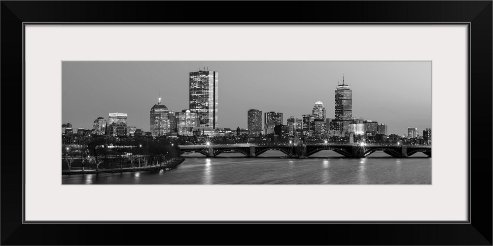 Panoramic view of the Boston City skyline illuminated at night, with the Longfellow Bridge in the foreground.