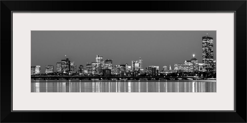 Panoramic view of the Boston City skyline at night, with lights reflected in the water.