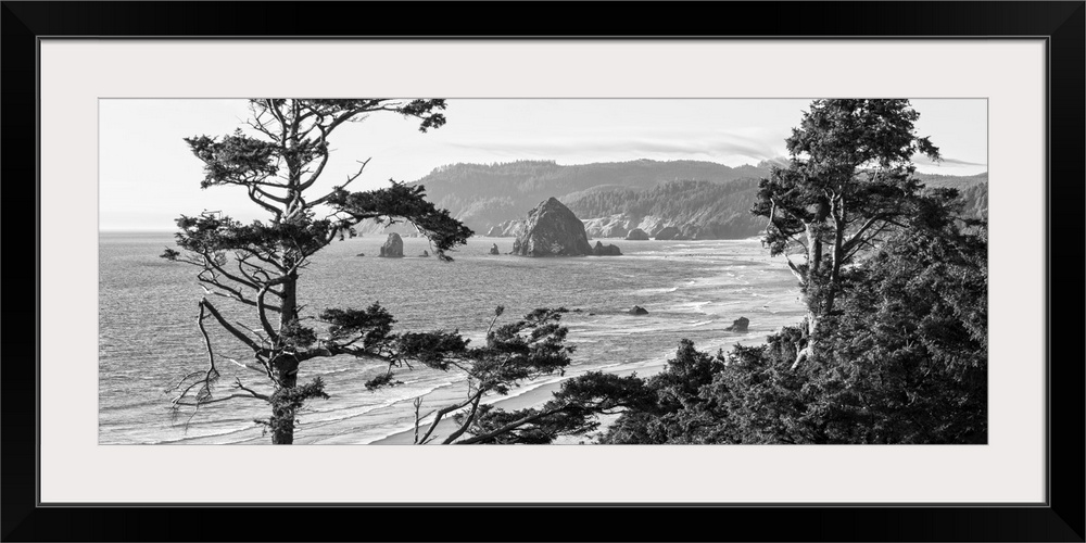 Black and white panoramic landscape photograph of Cannon Beach through the trees with Haystack Rock in the distance, Orego...