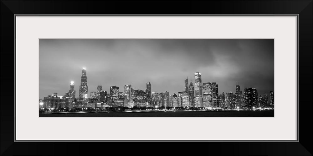 Panoramic view of the Chicago city skyline in the early evening, with city lights reflecting off the clouds above.