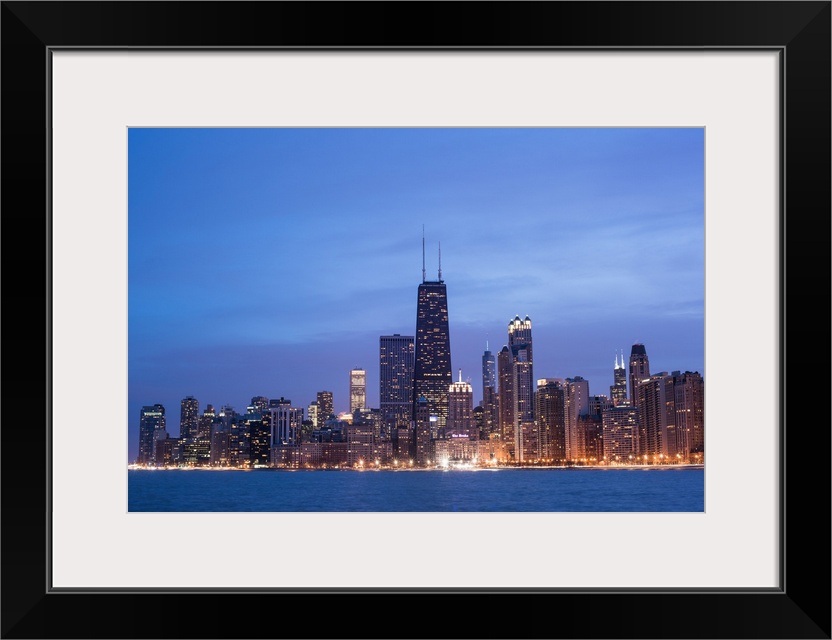 The Chicago city skyline illuminated in the early evening, seen from across the water.
