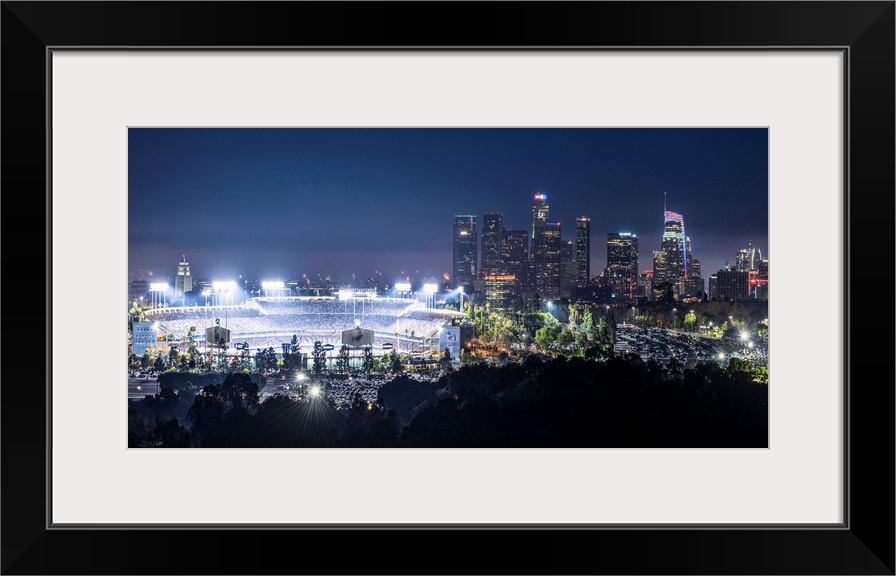 Photograph of Dodger Stadium lit up on a game night with the Los Angeles skyline on the right.