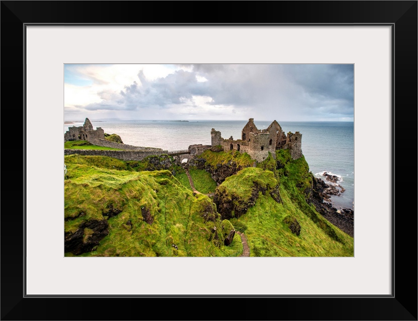 Landscape photograph of Dunluce Castle next to the ocean, taken from a higher point.