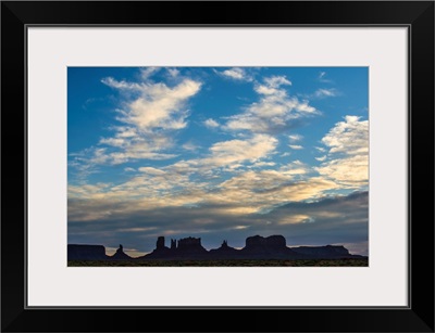 Fluffy Clouds Drift Over A Silhouette Of Rock Formations In Monument Valley, Utah