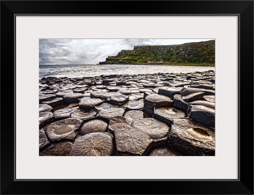 Landscape photograph of the basalt columns on Giant's Causeway with rocky cliffs and the Atlantic Ocean in the background.