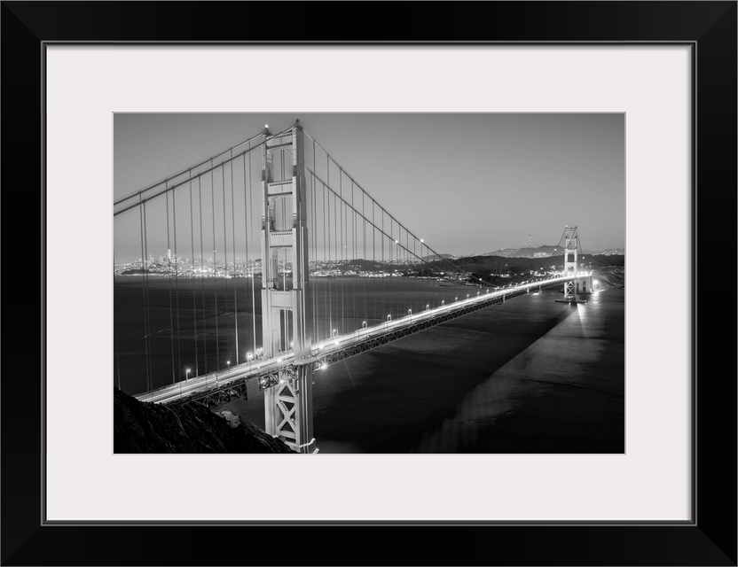 Cool toned photograph of the Golden Gate Bridge lit up at twilight with the city lights in the background.