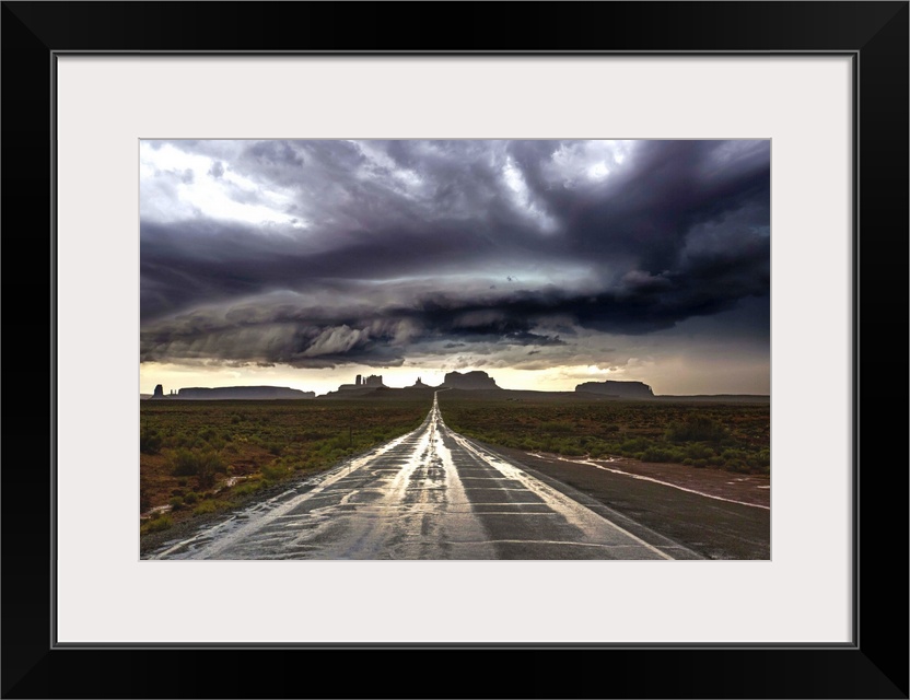 Photograph of Monument Valley with dramatic clouds above taken from a wet road after a storm.