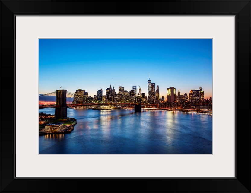 View of the New York City skyline at night with the Brooklyn Bridge, from across the water.