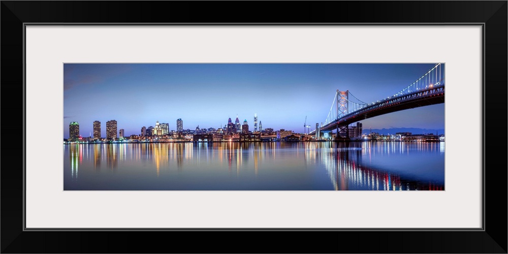 Panoramic photo of the Philadelphia city skyline reflected in the water at night, with the Benjamin Franklin Bridge on the...