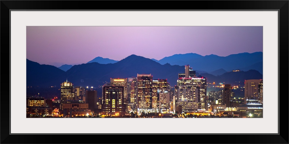 Panoramic photograph of a colorful sunset over the Phoenix, Arizona skyline with silhouetted mountains in the background.
